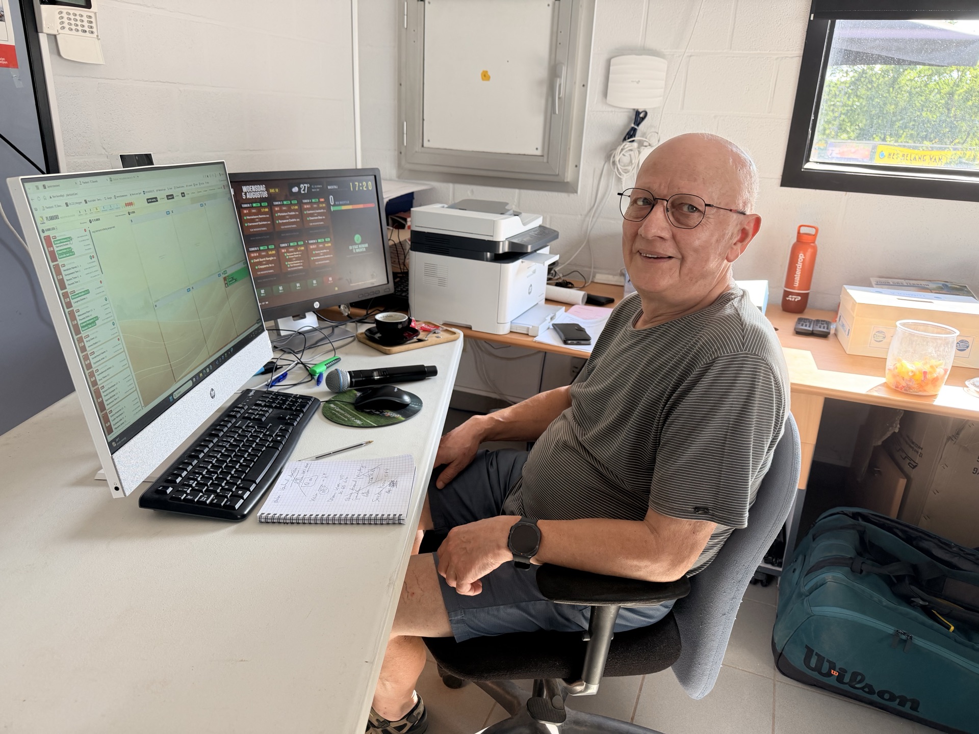 Marcel Schildermans aan zijn bureau, met het planbord op het ene scherm en het wedstrijdscherm op het andere